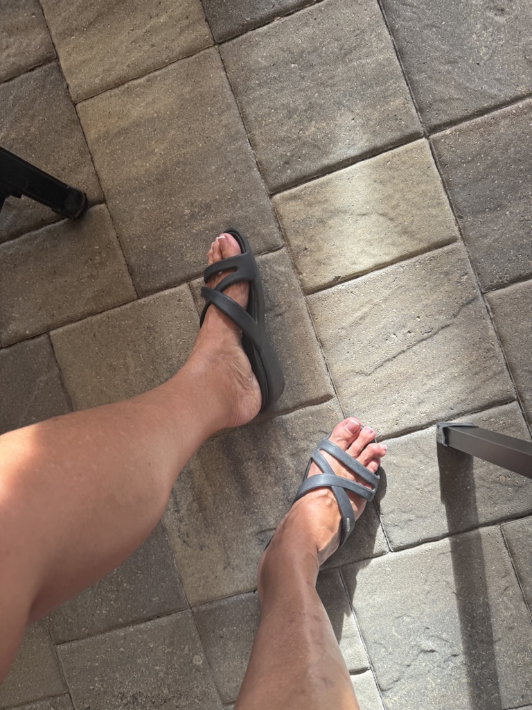 Feet in black crisscross sandals on pavers