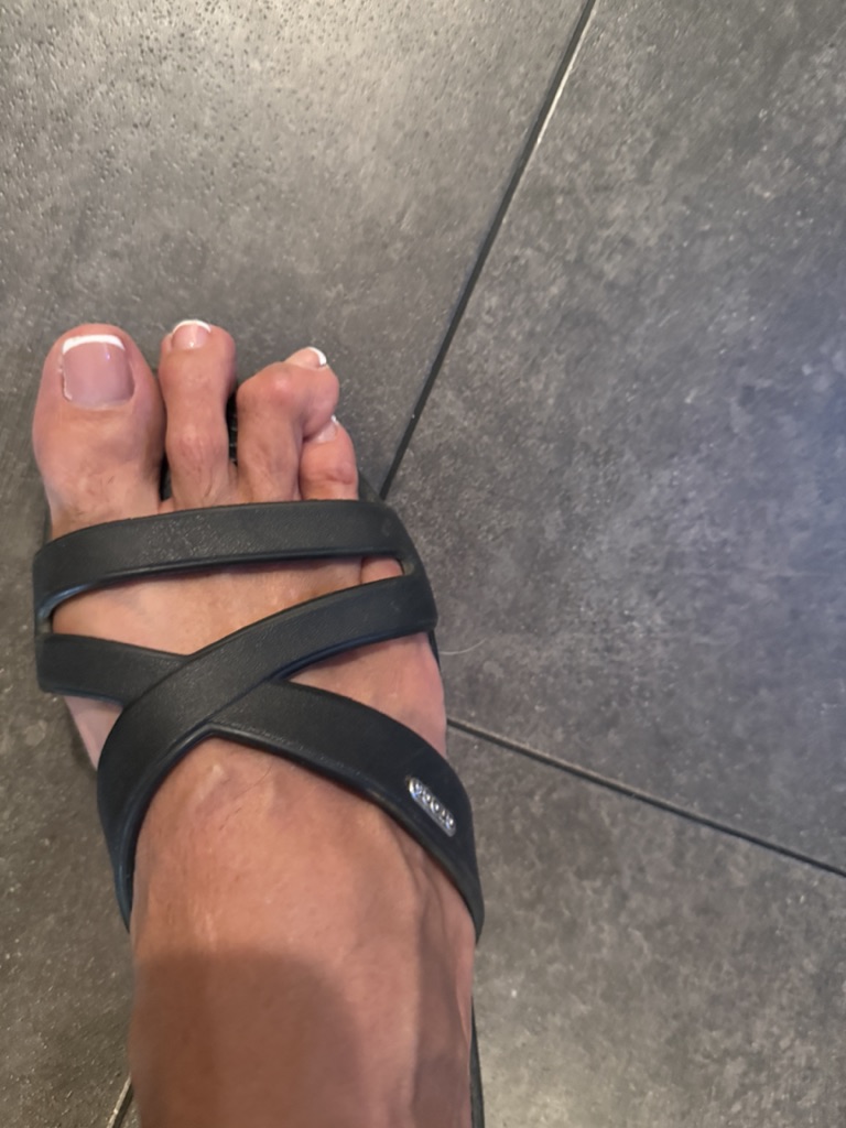 Foot in black crisscross sandal on gray tile