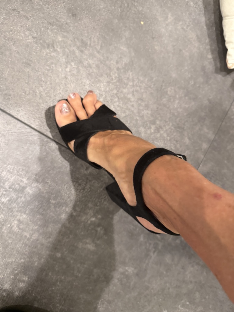 Foot in black heel sandal on gray tile